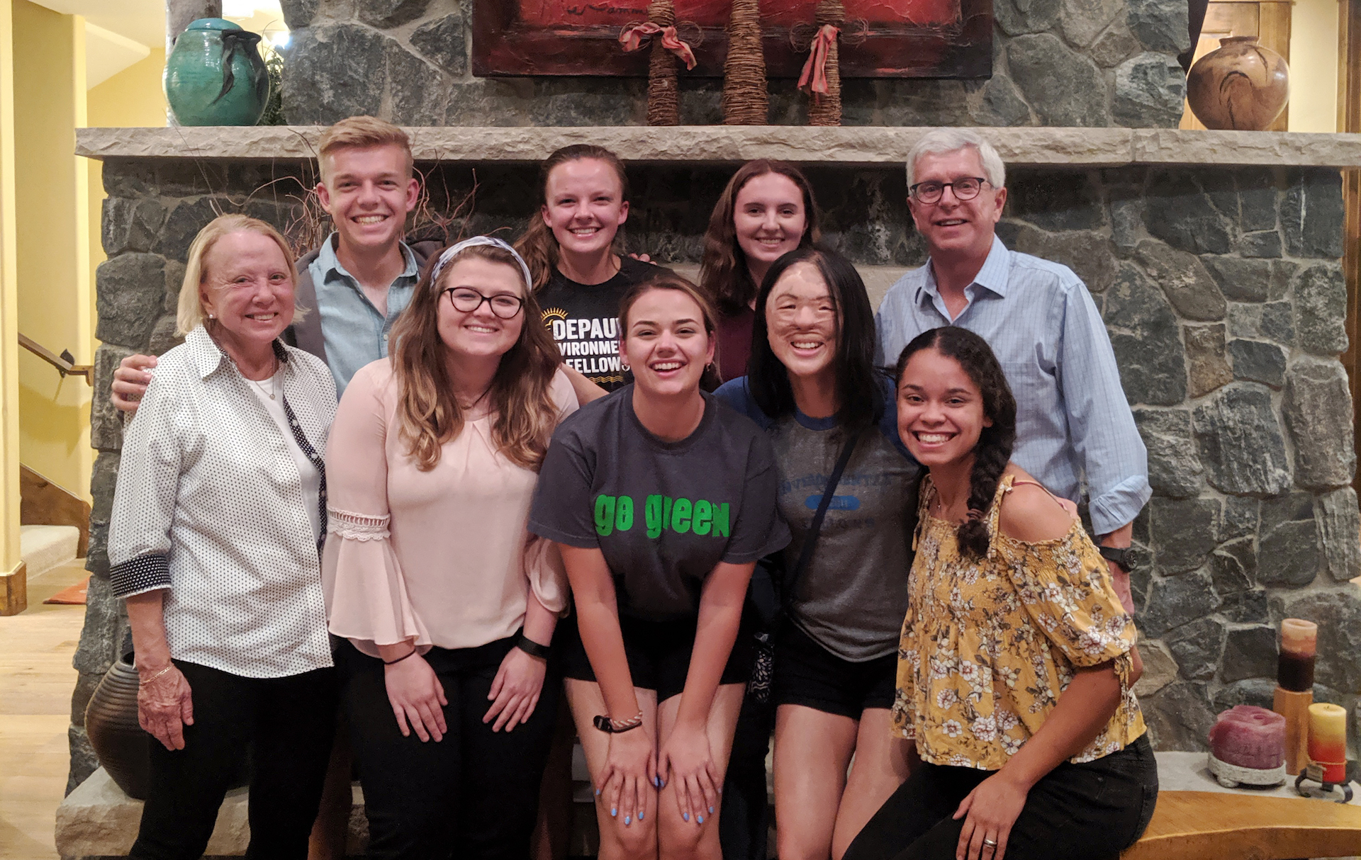 Students standing with alumni, the Peternells, in front of a fireplace. 