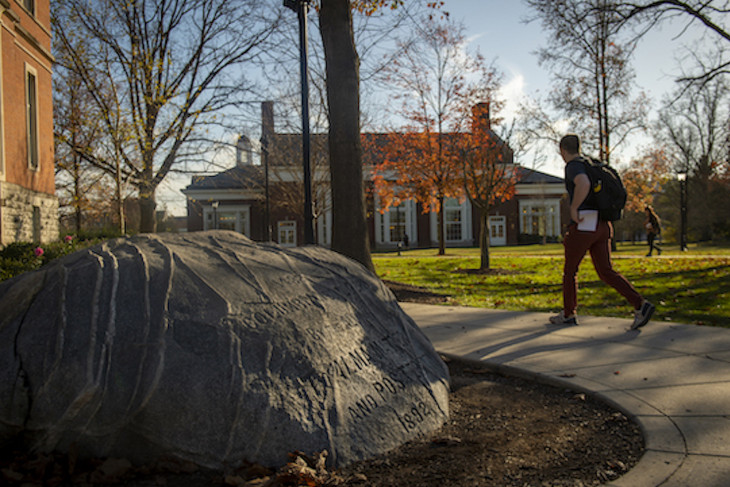 student walking past boulder on campus