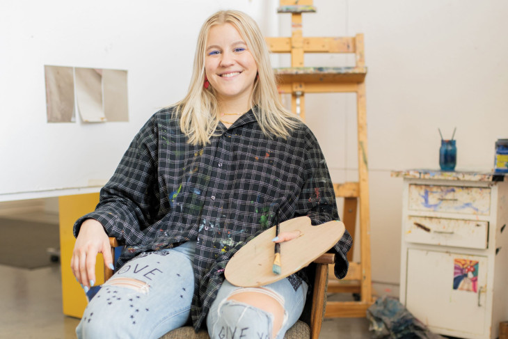 Student sits while holding art supplies