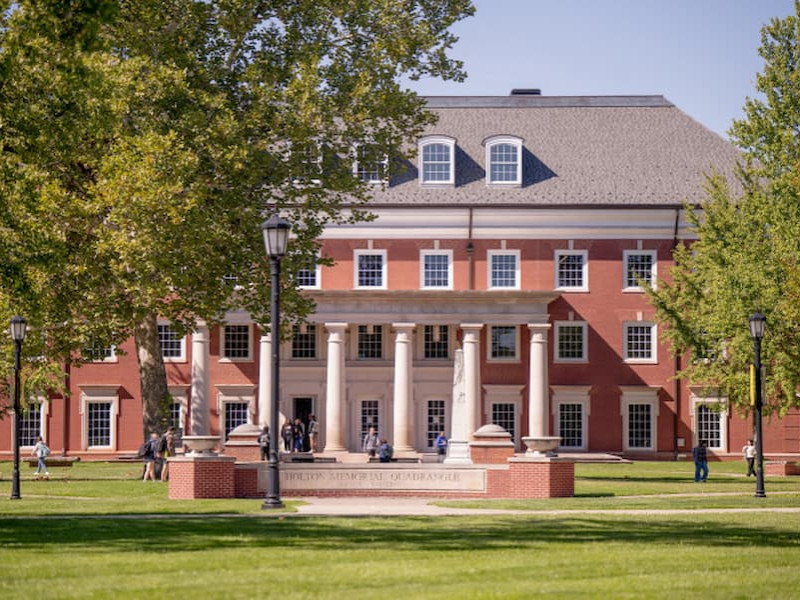 A multi-story brick university building with white pillars and a green lawn.