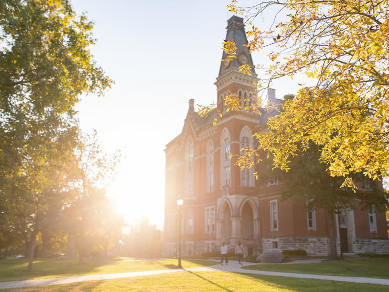 A historic brick university building with a clock tower during a bright sunset.