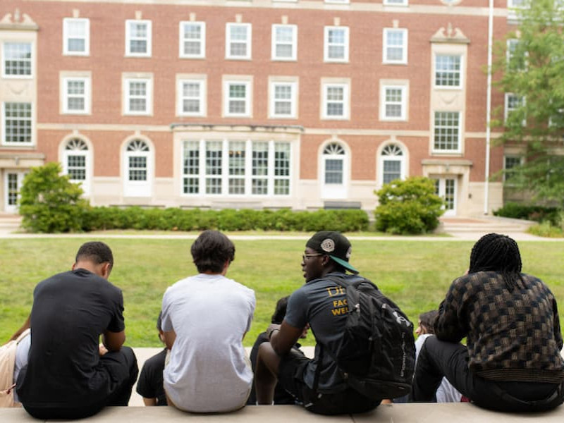 A diverse group of student residential assistants (RAs) smiling and posing together for a group photo outside on a brick campus pathway.