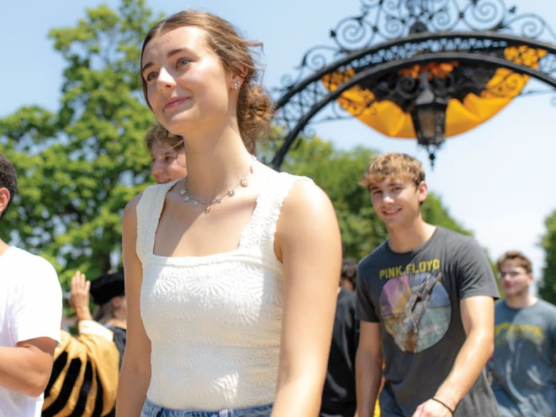 Smiling students walking on campus under a decorative archway during a university event.