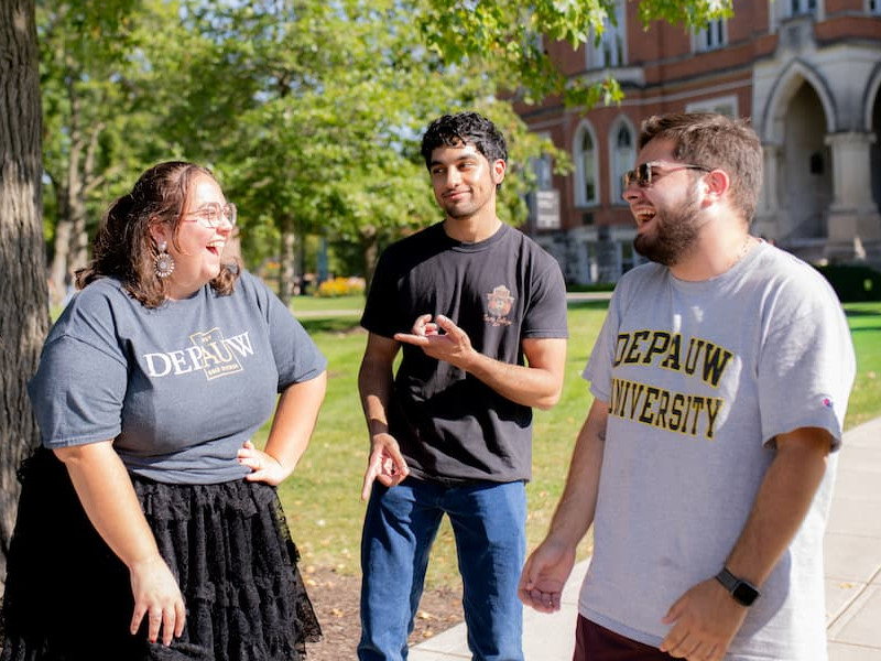 four students laughing outside under a tree