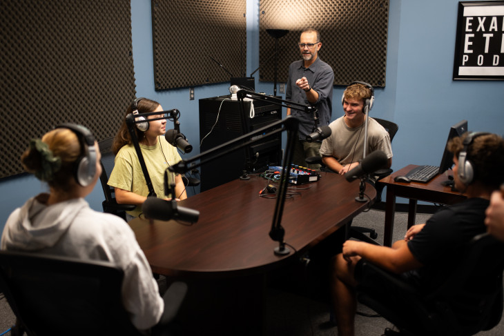 Students gather around a table in podcast studio
