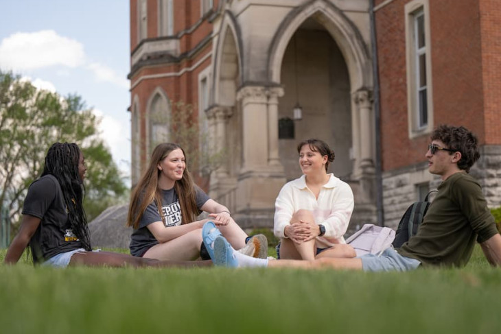Four students sitting on the grass in front of East College