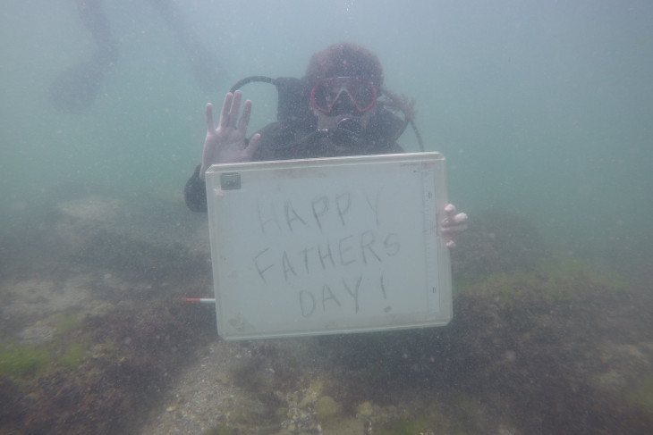 Caleb under water holding a sign that says happy fathers day 