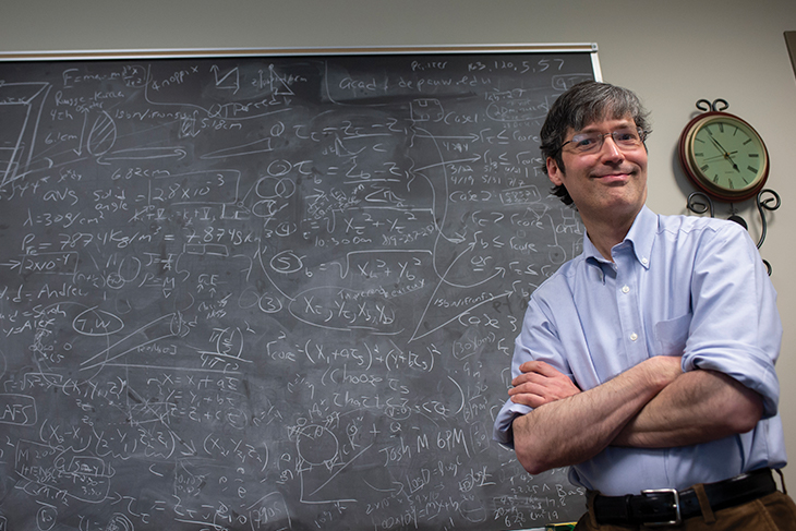 Alexander Komives stands before a chalkboard full of research data