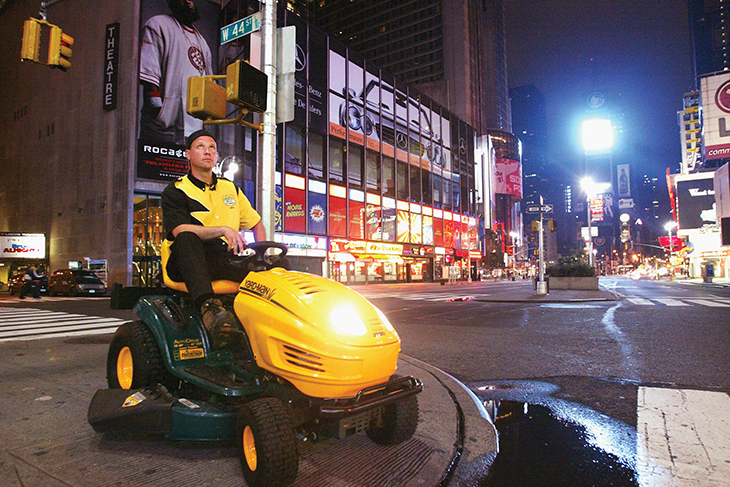 Brad Hauter ’87 sitting on a lawn mower in a city street