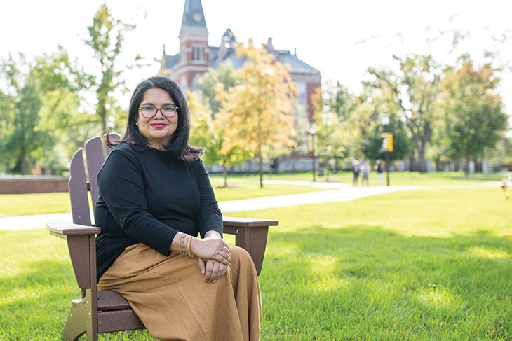 Deepa Prakash in an Adirondack chair in front of East College