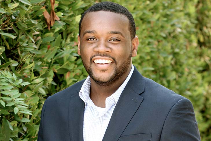 Headshot of Edward Garnes in a blue suit in front of green leaves