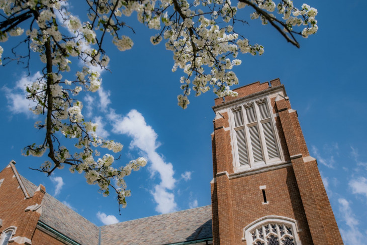 Vivid blue sky with apple blossoms in the foreground and a campus building in back