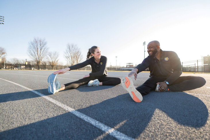 Two people stretch on the track