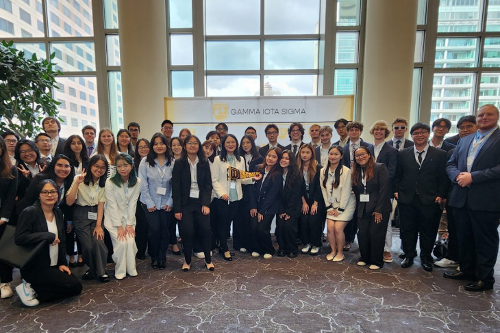 Professor of Business Analytics and Mathematical Sciences Zhixin Wu holds a a DePauw University flag while posing with student delegates for a photo at the 53rd Gamma Iota Sigma conference at the Indiana Convention Center on Sept. 26.