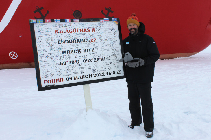 Tim Jacob stands near the ship that found the Endurance and a sign marking the spot