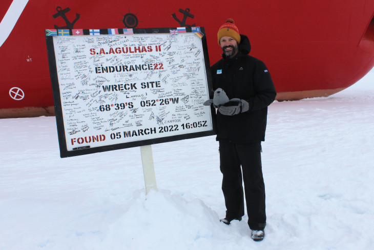 Jacob stands in front of ship at the site of discovery of Endurance