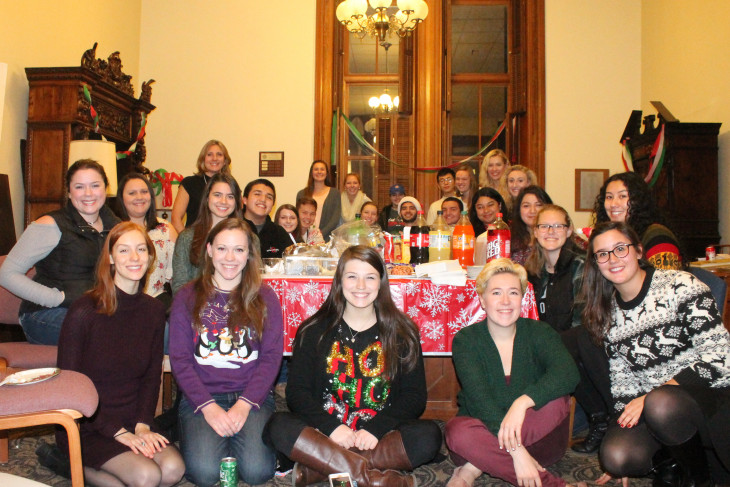 A group of students sitting around a snack table in Christmas sweaters.