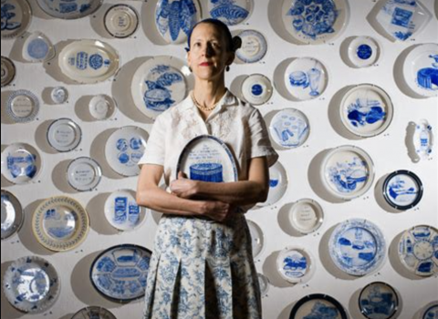 woman standing in front of wall with blue and white porcelain plate hung on it