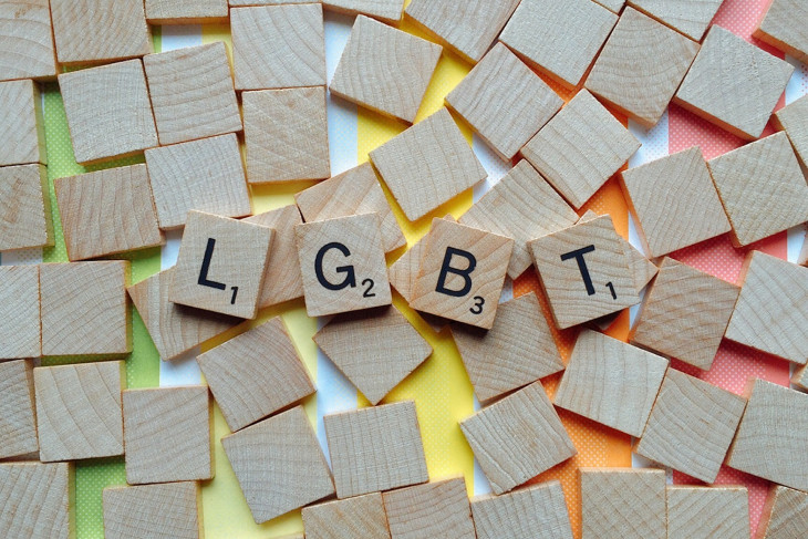 Scrabble pieces on a rainbow background, spelling out the letters LGBT