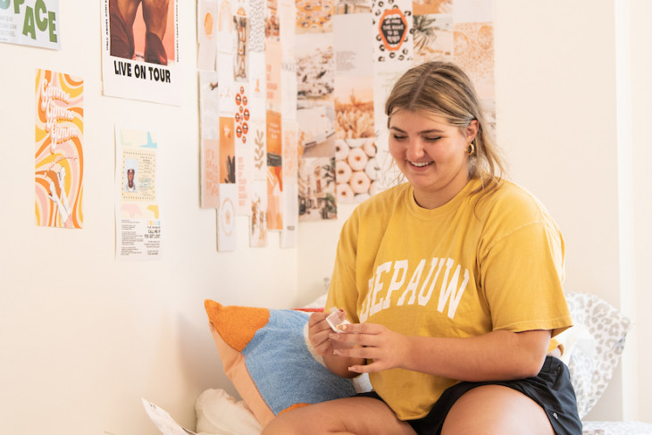 Student smiling sitting on her bed putting posters on the wall 