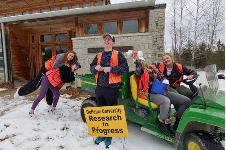 Students standing in snow with a sign that says research in progress