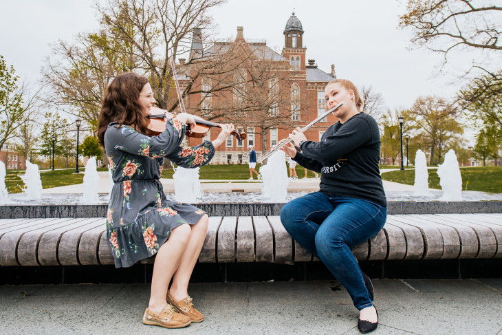 Music students playing in front of a water feature with East College in the background