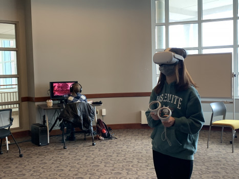Two students, one gaming on a desktop, one on a VR set.