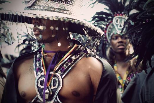 Man wearing celebratory attire, sequins and feathered hat.