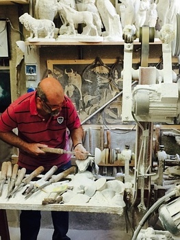 Man making pottery in a studio surrounded by sculptures