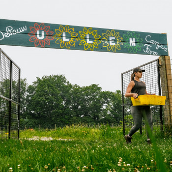 Student carrying a container at the entrance to the campus farm