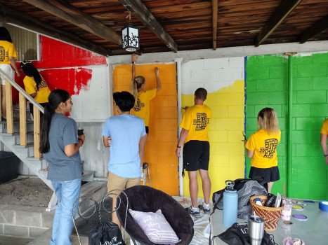 A group of DePauw students are painting a wall with bright rainbow stripes.