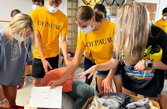 A group of DePauw students in bright yellow DePauw shirts are sorting through donated items.
