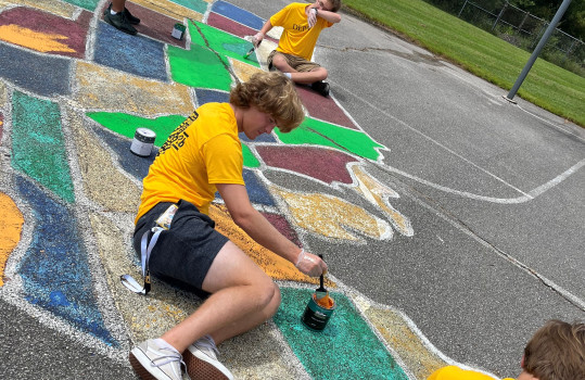A DePauw student is painting a basketball court with colorful paint.