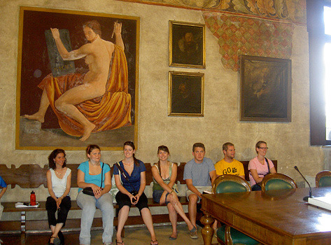 Students sitting on a bench with art on the wall in the background
