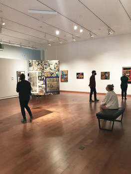 People standing and sitting in the lower level gallery looking at artwork