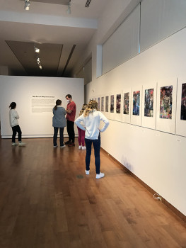 People looking at a row of prints and other people standing and talking