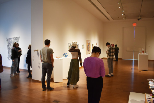people standing in gallery exhibiting student artwork 