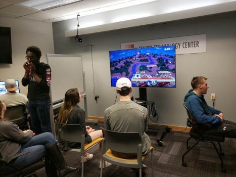 Several students gathered around a large monitor as they play Super Smash Brothers