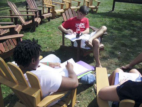 Students sitting in wooden lawn chairs outside a residence hall