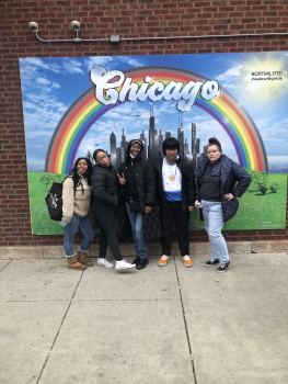 A group of students are standing in front of a banner with a rainbow and the word "Chicago" on it. They are making goofy faces.