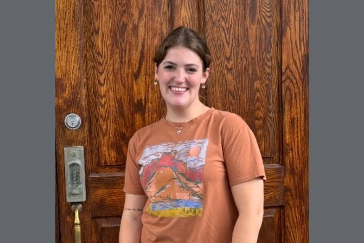 Photo of Elly standing in front of a wood-paneled wall