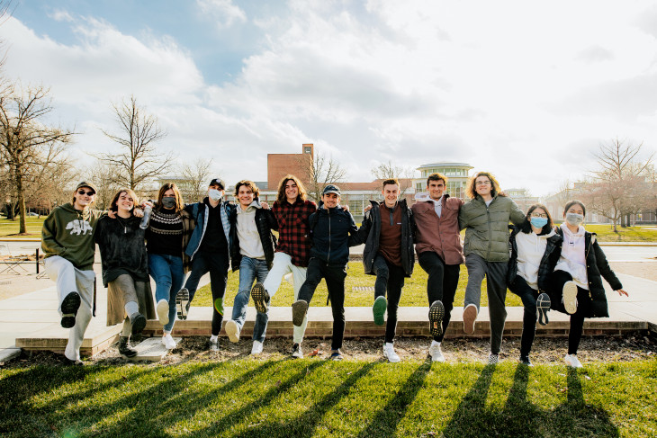 Students kicking one leg up in front of Green Center
