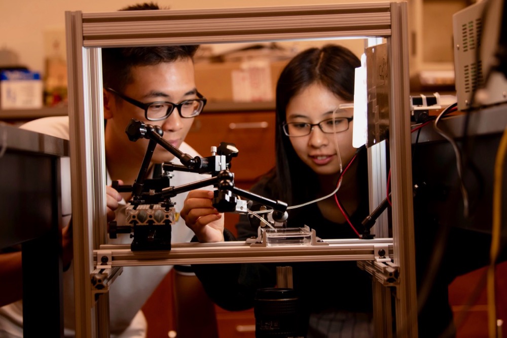 Two students look over a water droplet preparing to drop.