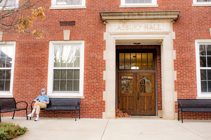 masked man sits outside Asbury Hall in the fall 