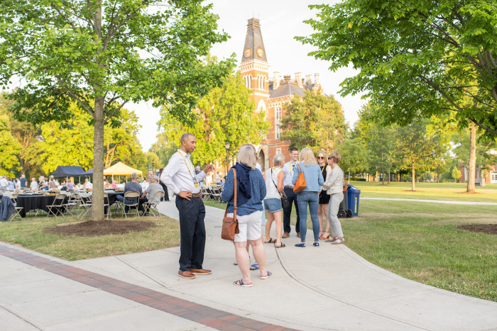 Alumni talking during a reunion event with East College background