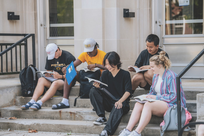 Four students seated on the stairs in front of Harrison hall, during an outdoor class lecture