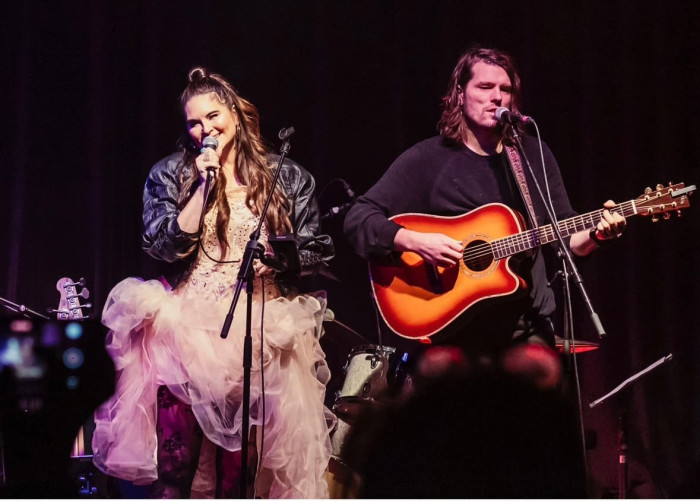 male and female on stage with guitar on stools
