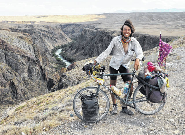 Luke Miller standing with his bicycle with a scenic canyon background