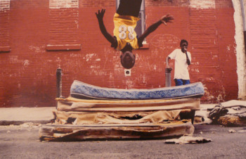 Mattress Flip by Zoe Strauss depicts a little boy doing a flip on a mattress, while another little boy is watching