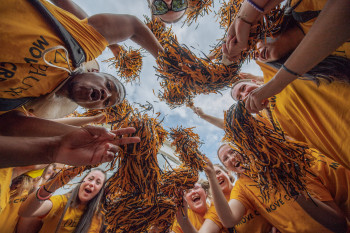 Students grouped together in a circle cheering with pom poms